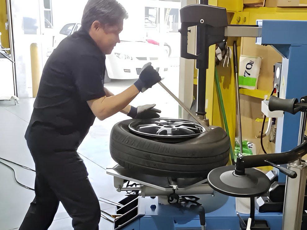 店主がタイヤチェンジャーを操作し、ホイールに新しいタイヤを慎重に組み込んでいる作業風景
